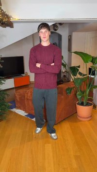 Μπορντό πουλόβερ με πλέξη καλώδιο, γκρι παντελόνι και ασημένια αθλητικά παπούτσια. Εσωτερικός χώρος με γλαστράκι και καφέ καναπέ στο παρασκήνιο. Ξύλινο πάτωμα.