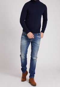 Námořnický rolák v kombinaci s vybledlými modrými džíny. Hnědé semišové kotníkové boty dotvářejí outfit a dodávají mu ležérní vzhled.