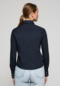 Camisa de manga larga azul marino hecha de tejido suave, con cuello clásico y puños abotonados. Ajuste entallado con aberturas laterales.