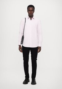 Svetlo roza, prugasta majica z dolgimi rokavi, črne slim-fit hlače in črne čevlje. Model drži majhno črno torbico preko telesa.