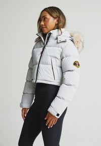 Gaiša pelēka pūkaina jaka ar kažokādas apdari kapuci, melniem rāvējslēdzējiem un plecu uzlīmi. Iezīmes ir elastīgi piedurkņu gali un rāvējslēdzēja kabata.