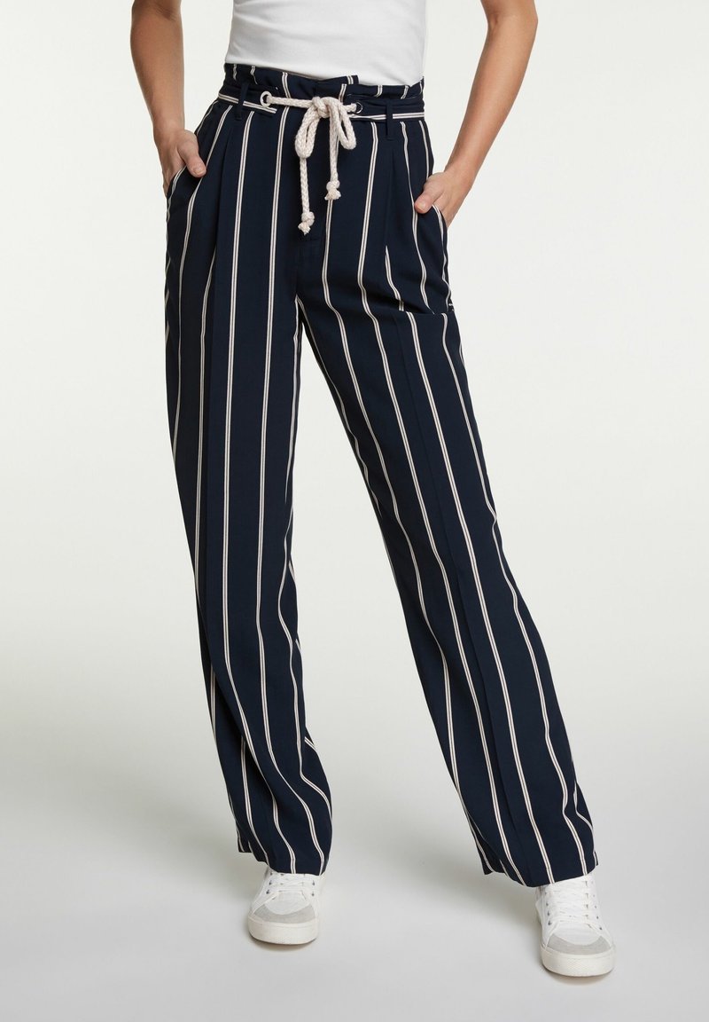 Pantalon bleu marine à rayures verticales blanches, ceinture en corde, poches latérales, porté avec des baskets blanches et un haut blanc rentré.