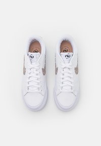 Bílé tenisky s texturovaným, tkaným vzorem na bočních stranách, ploché tkaničky, polstrované límce a krémově zbarvené vnitřní podšívky.