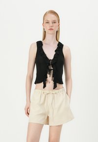 Svart cropped topp med flate kanter og V-hals, med en knytedetalj foran. Kombinert med beigefargede shorts med snøring. Enkelt, avslappet design.