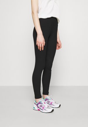 Black ribbed leggings with a fitted design, paired with white sneakers featuring purple and turquoise accents.