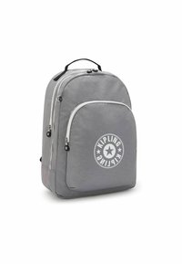 Sac à dos gris avec une texture lisse, présentant un grand logo à l'avant, deux compartiments zippés et une poignée supérieure pour un transport facile.