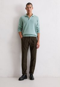 Jasnoturkusowy dzianinowy sweter polo z kołnierzykiem i trzema guzikami, zestawiony z ciemnobrązowymi spodniami i czarnymi sznurowanymi butami.