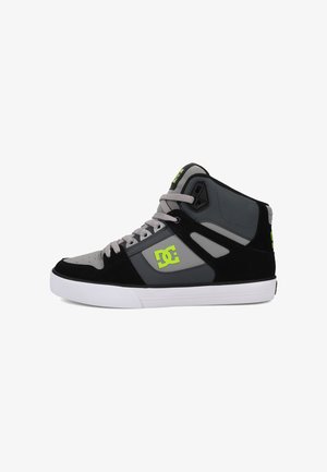 Zapatillas medianas en negro y gris, hechas de ante y materiales sintéticos, con un logo en verde lima y una suela de caucho blanca. Diseño de puntera perforada.