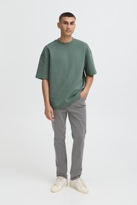 Roheline puuvillane lahtine T-särk lühikeste varrukatega, sobitatud hallide teksapükste ja beežide tossudega. Lihtne disain, pehme tekstuur.