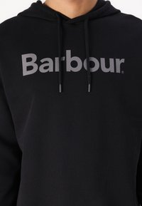 Hanorac negru cu glugă, confecționat din bumbac, având un mare logo gri "Barbour" pe față, cu șnururi de ajustare și o croială lejeră.