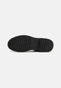 Suela de zapato de goma negra con una superficie texturizada, que presenta ranuras horizontales para tracción y una forma redondeada en la punta.