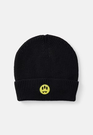 Berretto lavorato a maglia nero con una texture a coste. Presenta un viso sorridente giallo ricamato con zanne al centro del bordo ripiegato.