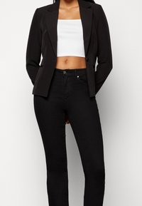Czarna marynarka o strukturalnym kroju i klapkach, zestawiona z dopasowanymi czarnymi dżinsami. Całość uzupełnia prosty biały krótki top pod spodem.