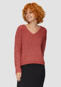 Roter Strickpullover mit V-Ausschnitt, der ein strukturiertes Muster aufweist, lange Ärmel und eine lockere Passform hat. Kombiniert mit einem schwarzen Rock.
