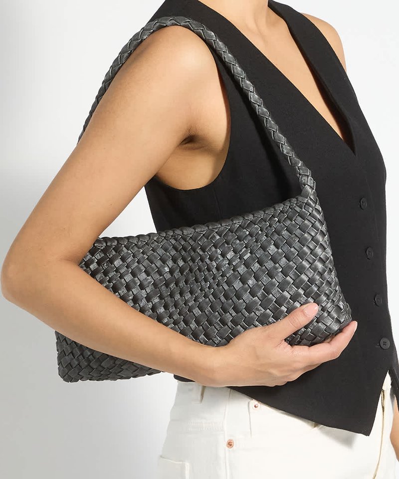 Femme portant un haut noir sans manches et un pantalon blanc porte un sac à bandoulière noir tissé avec une bandoulière tressée sur son bras.