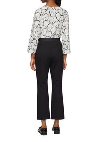 Blouse blanche avec motif floral noir, manches larges ; associée à un pantalon évasé noir et des chaussures noires. Tissu lisse et taille ajustée.