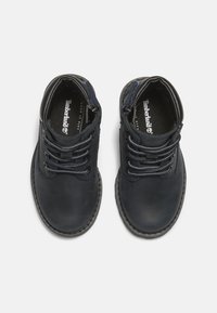 Botas de cuero oscuro de tobillo en color azul marino, con puntera redonda, ojales metálicos y cordones bicolor, que cuentan con una suela de goma cosida. Logo de Timberland en la plantilla.