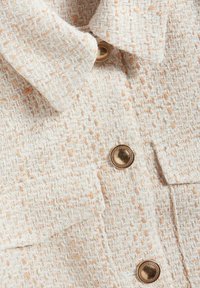 Tweed jasje in crèmekleur met subtiele perzikkleurige stippen, met een geknipt kraag en goudkleurige knopen. Gelaagde stof met een geweven patroon.