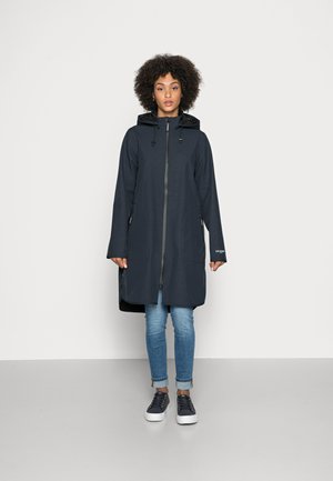 Long dark blue coat with a hood, featuring a front zipper and two side pockets, worn over light blue jeans and sneakers. Smooth fabric texture.