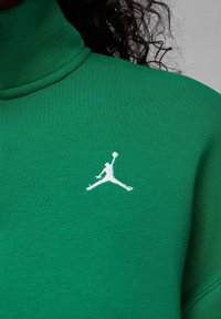 Zielona bluza z wysokim kołnierzem i prążkowanym kołnierzykiem, z białym haftowanym logo Jumpman na lewej piersi. Miękki bawełniany materiał.