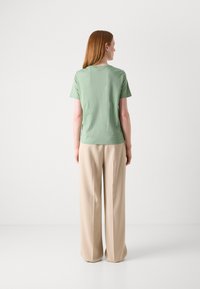 T-shirt in cotone verde chiaro con maniche corte, collo a giro e vestibilità rilassata, abbinata a pantaloni beige a gamba larga.