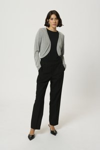 Silver cropped cardigan over a black top, paired with high-waisted black trousers and pointed black shoes. Smooth textures, fitted design.