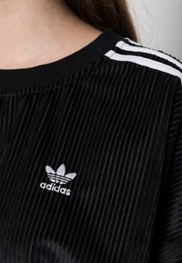 Černé žebrované tričko s kulatým výstřihem, s bílými pruhy adidas na ramenou a bílým logem adidas na hrudi.