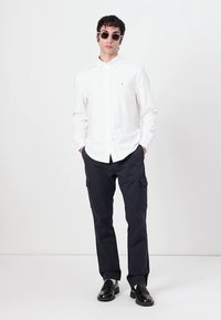 Witte overhemd met knopen, marineblauwe cargobroek, zwarte zonnebril en zwarte schoenen. Het overhemd heeft een gladde textuur; de broek heeft steekzakken.
