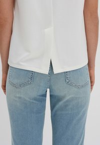 Camicia bianca con orlo posteriore spaccato, abbinata a jeans azzurri chiari con tasche posteriori e morbido tessuto denim.