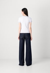 Witte kortemouwtop met lichtblauwe bies, gecombineerd met donkerblauwe wijde jeans met gestikte achterzakken. Minimalistisch ontwerp.