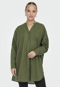 Chemise boutonnière vert olive avec un col en V, deux poches poitrine et des manches longues. Fabriquée dans un tissu lisse avec une coupe décontractée.
