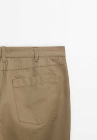 Dos d'un pantalon beige montrant une seule poche arrière et des passants de ceinture sur fond blanc.