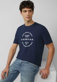 Marineblauwe katoenen T-shirt met korte mouwen, met een wit cirkelvormig tekstontwerp met de tekst "S. Oliver A.R.R." en casual slogans in het midden.