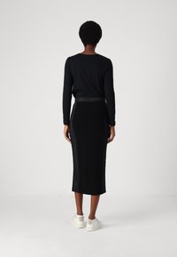 Zwarte lange mouwen top met een ronde hals, gecombineerd met een zwarte strakke midirok. De outfit heeft een tonale tailleband en witte sneakers.