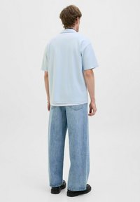 Lichtblauw, kort mouwen polo shirt met een gestructureerd patroon, gedragen met een loszittende lichtblauwe spijkerbroek en zwarte platform schoenen.