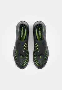 Black athletic shoes featuring a sleek design with green accent lines. The upper material is textured, with a minimal lacing system.