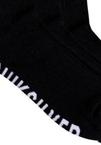 Black socks made of soft fabric feature a white logo along the cuff. The design is simple with a smooth texture and elasticated opening.