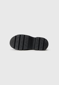 Sort sneakersål med en tekstureret gummi mønster, der har horisontale og diagonale riller for greb og stabilitet.