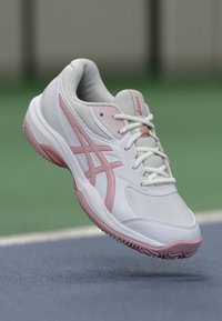 Weiße Sportschuh mit pinken Akzenten, strukturiertes Mesh-Obermaterial, Schnürdesign und Gummisohle mit einer gemusterten Lauffläche für Traktion.