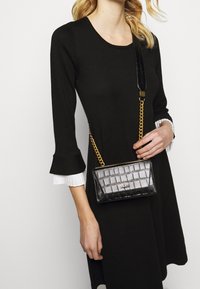 Borsa a tracolla in pelle sintetica effetto coccodrillo nera con tracolla a catena dorata, caratterizzata da una forma rettangolare e dal logo DKNY in rilievo sulla parte anteriore.