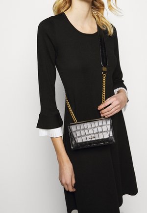 Černá kabelka přes rameno z umělé krokodýlí kůže se zlatým řetízkovým popruhem, s obdélníkovým tvarem a vyraženým logem DKNY na přední straně.