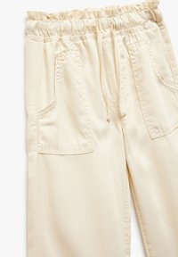 Pantaloni color crema con cintura elastica, chiusura con cordoncino e due tasche anteriori cucite. Tessuto liscio con una consistenza morbida.