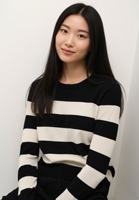 Black and cream striped sweater made of knit fabric, featuring long sleeves and a ribbed neckline, worn with dark pants.