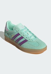 Mintgrön mockaskor med lila ränder, texturerade detaljer på tungan och en gummisula. Har snörning och vadderad krage.