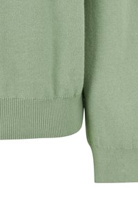 Gros plan d'un pull en maille vert clair montrant l'ourlet et les poignets côtelés avec un tissu doux et à texture fine.