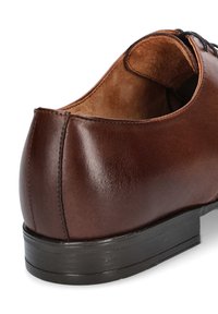 Brązowy skórzany but o gładkim wykończeniu, zaokrąglonym obcasie i kontrastowej czarnej gumowej podeszwie z teksturowanymi detalami.