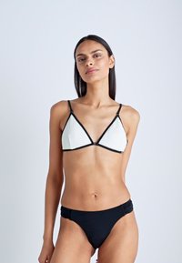 Zwart-wit bikini; top heeft driehoekige cups met een textuurpatroon en zwarte trim; het broekje heeft geraffineerde details in zwarte stof.
