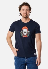 Navyblaues Baumwoll-T-Shirt mit einem Motiv eines Hundes in Kopfhörern und einer orangefarbenen Mütze. Rundhalsausschnitt und kurze Ärmel. Bequemer Schnitt.