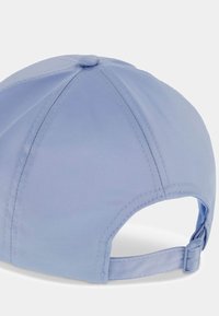 Gorra de béisbol azul claro vista desde atrás con correa ajustable y diseño de panel cosido sobre un fondo liso.