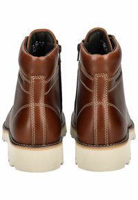 Botas de cuero marrón hasta el tobillo con suelas de goma blanca. Sus características incluyen costuras en contraste y una cremallera lateral para un acceso fácil.